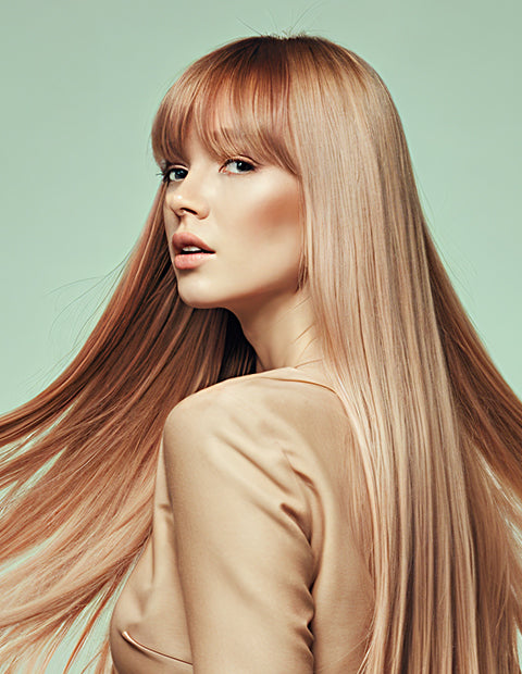 Person with long, straight, light brown hair and bangs, wearing a beige top, against a pale green background.