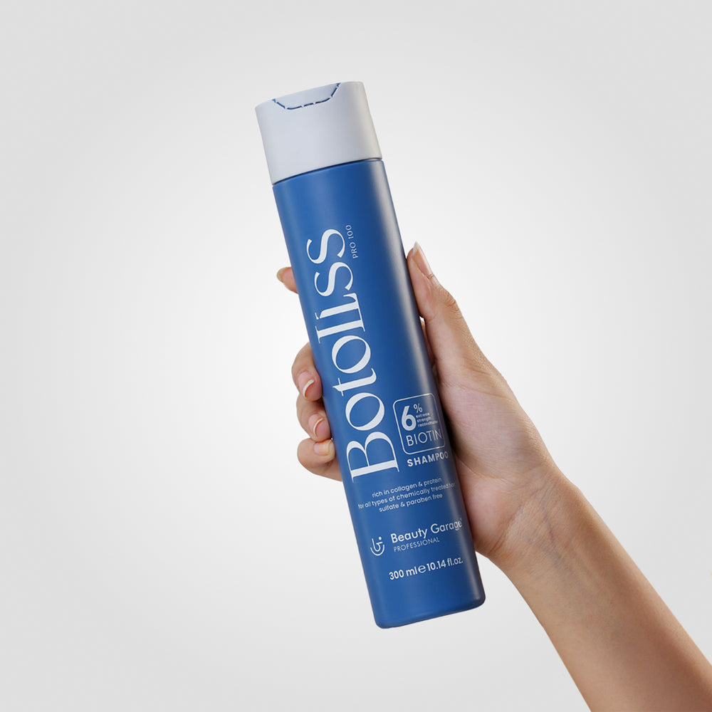 "Botoliss Biotin Shampoo" with a white cap is elegantly placed on a white surface, set against a light gray backdrop.