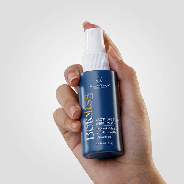 A hand holds a blue bottle of Botoliss Gloss Like Shine Spray by Beauty Garage.