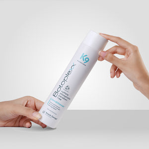 Two hands holding a sleek white bottle of Botoplexx K9 conditioner against a plain background.