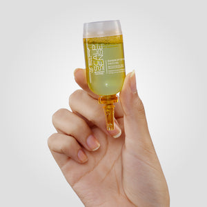 A hand holds a container of yellow liquid labeled "ScalpSense Dandruff Defense Vaccine" against a plain background.