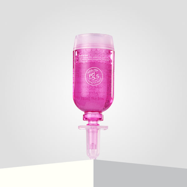 A pink bottle of ScalpSense Hairfall Defense stands upside down on the corner of a white surface.