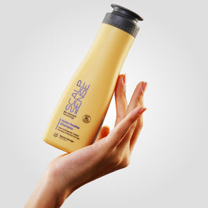 A hand holds a yellow bottle of ScalpSense Hydra Soothe Shampoo against a light background.