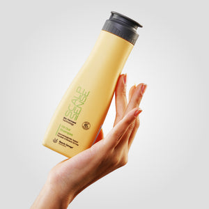 A hand holding a yellow bottle of ScalpSense Oil Out Shampoo against a light gray background.