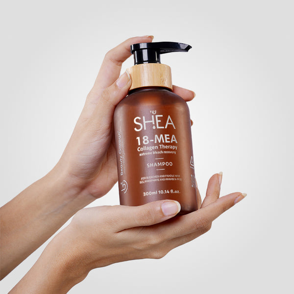 Two hands gracefully cradle a bottle of Shea-18 MEA Collagen Therapy Shampoo against a simple backdrop.