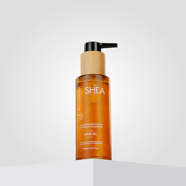 A brown bottle with a wood-textured pump labeled "Shea Hair Oil" stands against a white gradient background.