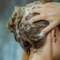 Person washing their hair with shampoo, forming a lather with their fingers massaging the scalp.