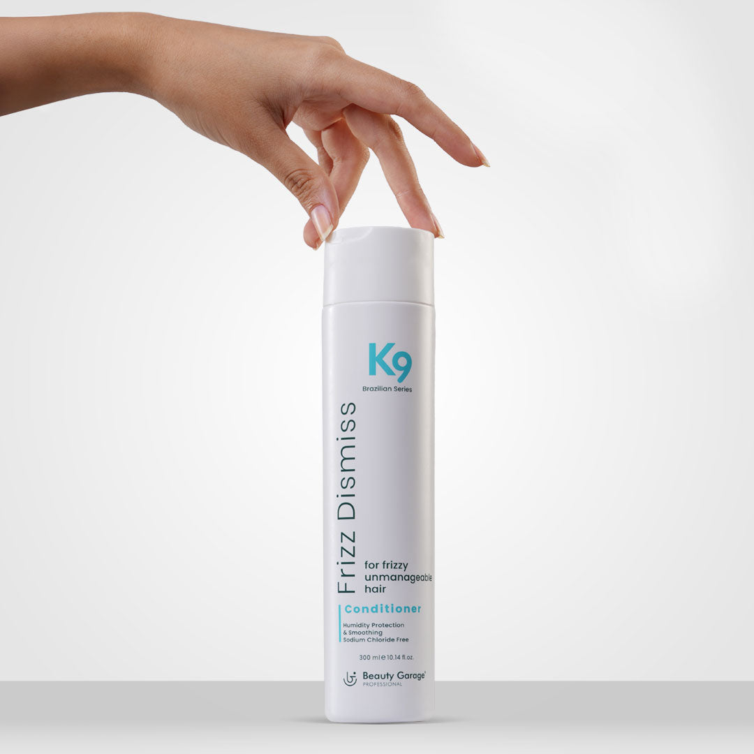 A hand holds a white bottle labeled "K9 Frizz Dismiss Conditioner," enriched with Botoplexx, against a chic gray background.