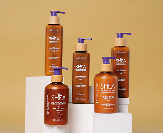 Five brown bottles of the Shea Curl Kit with blue pumps are displayed on white platforms against a beige background.